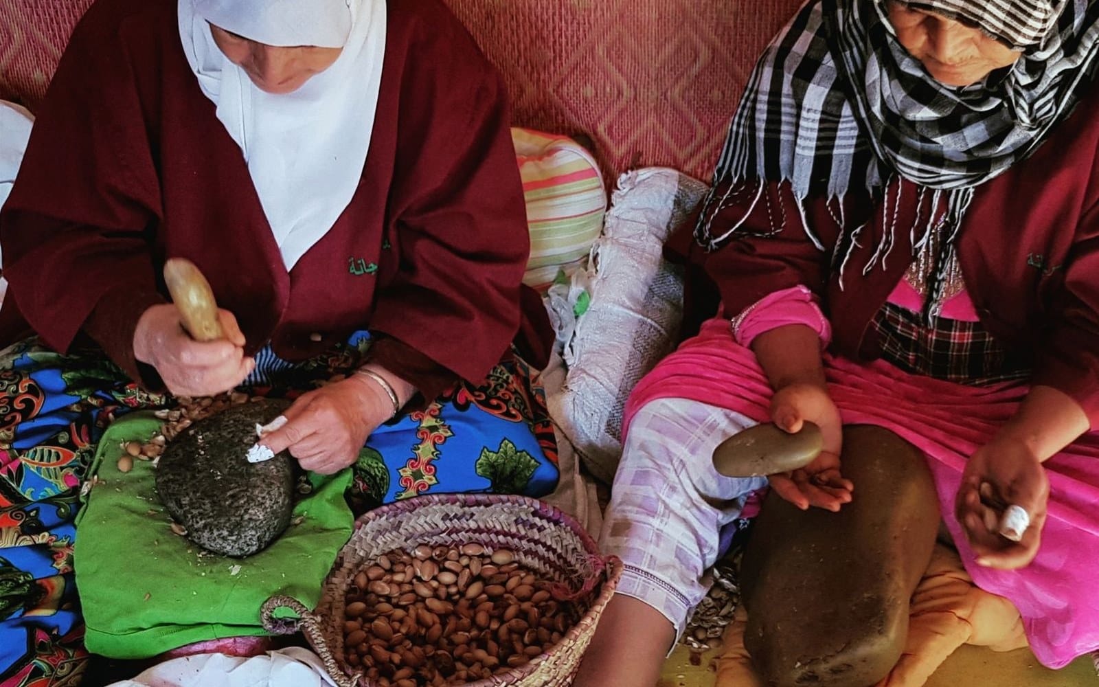 Two women cracking argan nuts by hand at a cooperative, the stop that appears on most desert itineraries