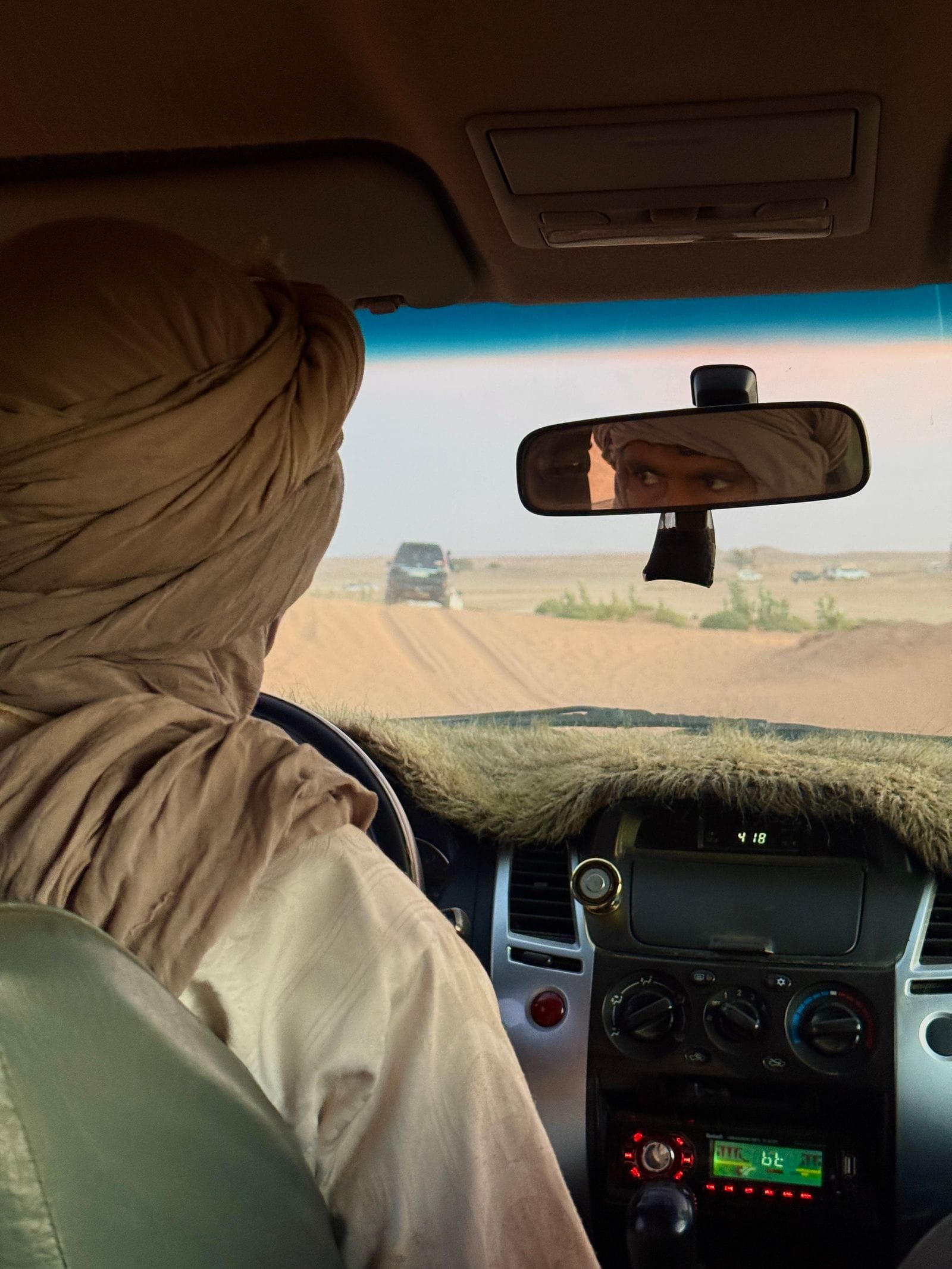 The view from a passenger seat of a desert 4x4, the driver at the wheel and a second vehicle ahead on the piste