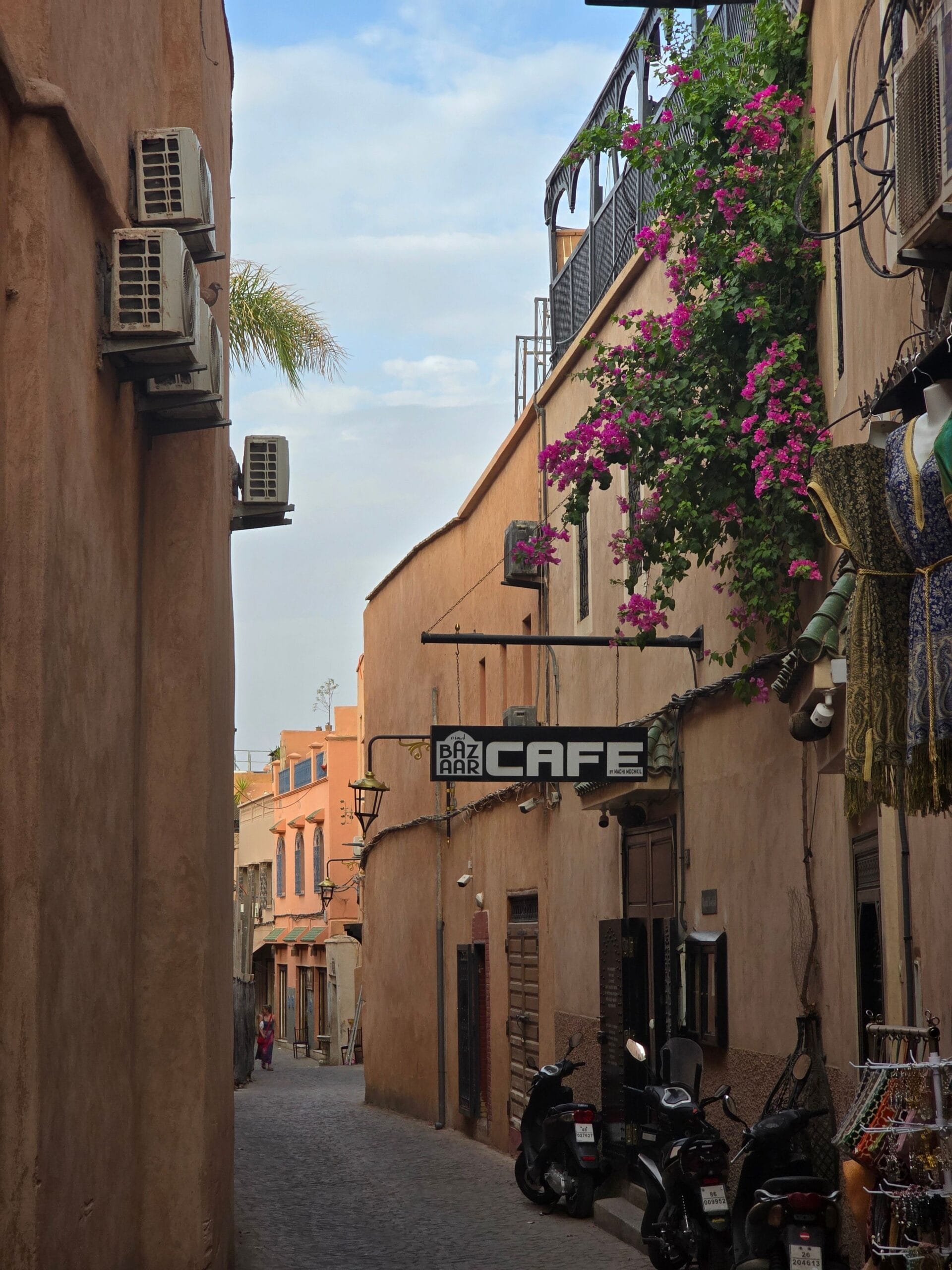 A quiet lane in the Marrakech medina, pink earth walls, bougainvillea over a balcony and a café sign