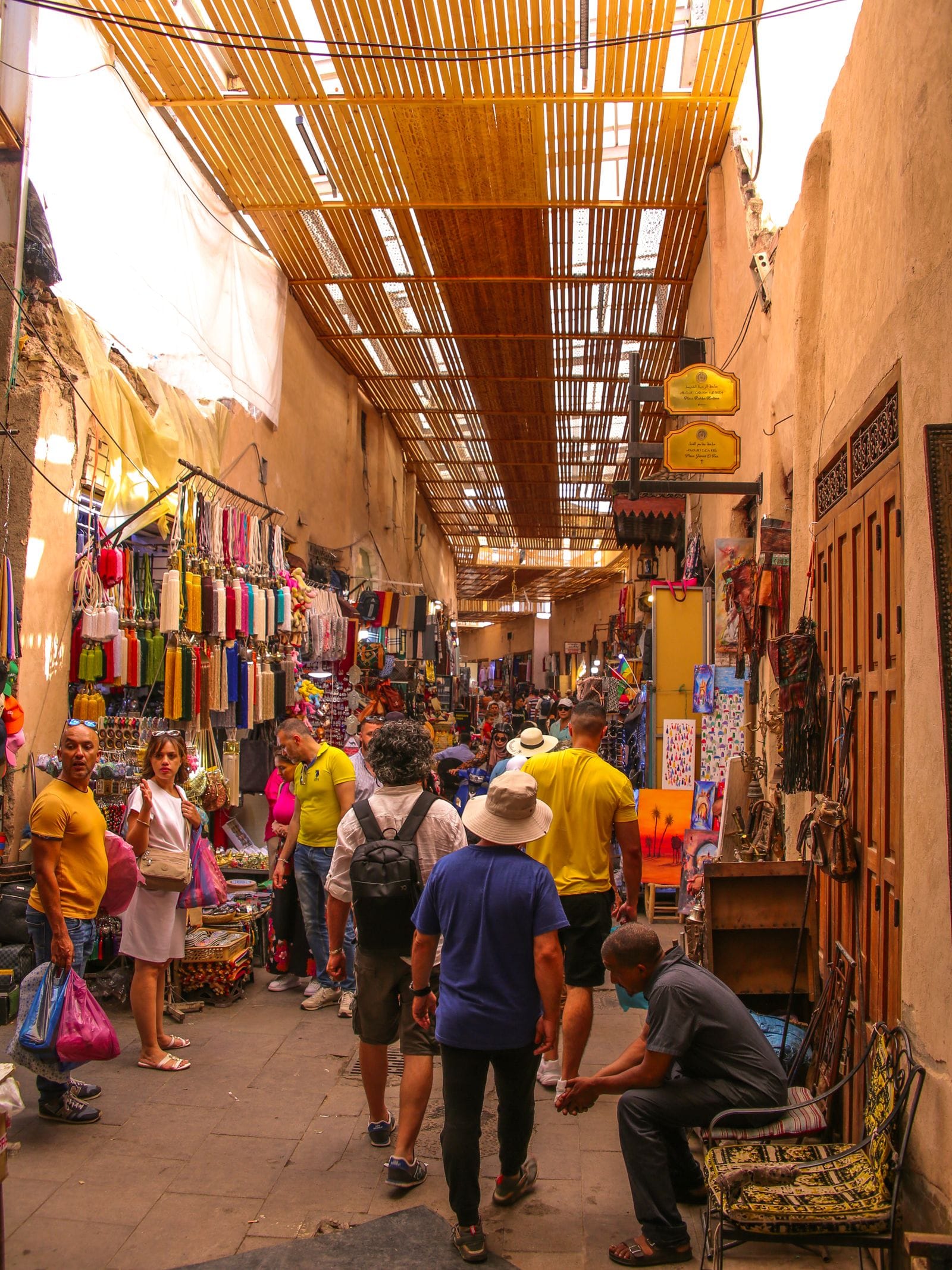 A busy covered street in the Marrakech medina, lined with shops and signage, where most Sahara tours are actually sold