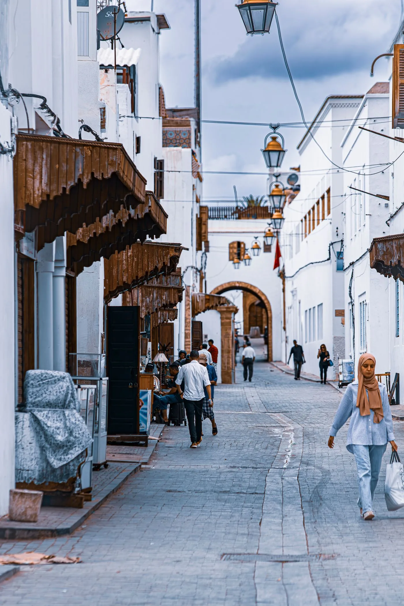 A quiet Moroccan street of whitewashed buildings with people going about daily life