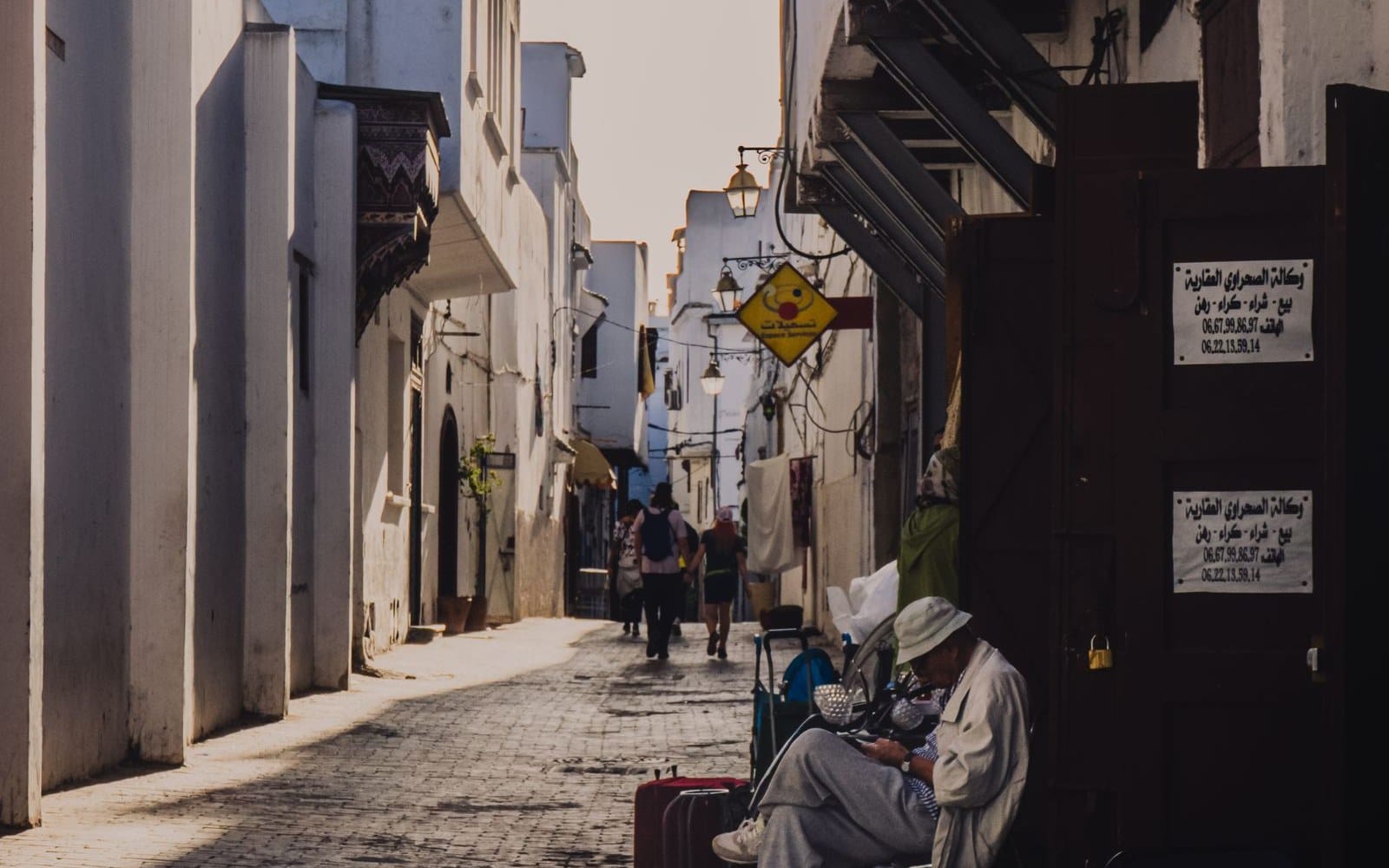 A street in the Rabat medina, an estate agency sign on the door and a suitcase on the pavement