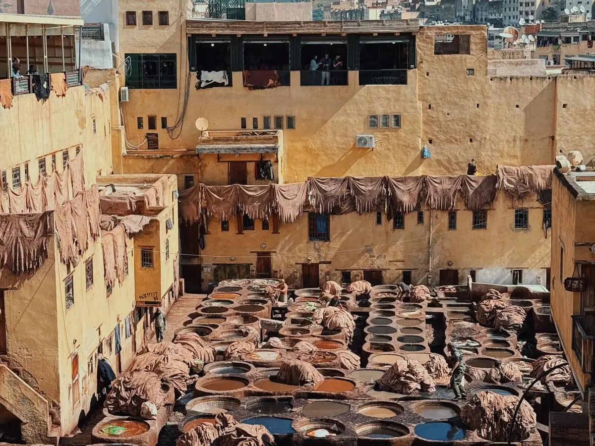 Visitors on a leather-shop terrace above the dye pits of the Chouara tannery in Fes, the view that is free and the exit that is not